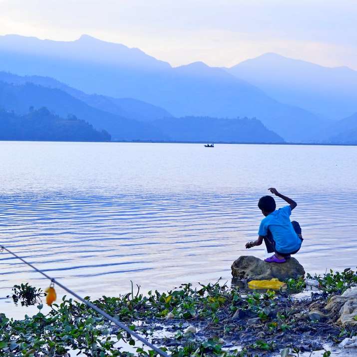 Frau im blauen Hemd sitzt auf Felsen am Meer Schiebepuzzle online