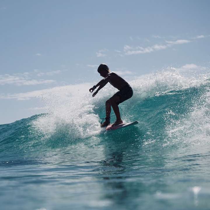 Hombre en traje de neopreno negro surfeando sobre las olas del mar durante el día puzzle deslizante online