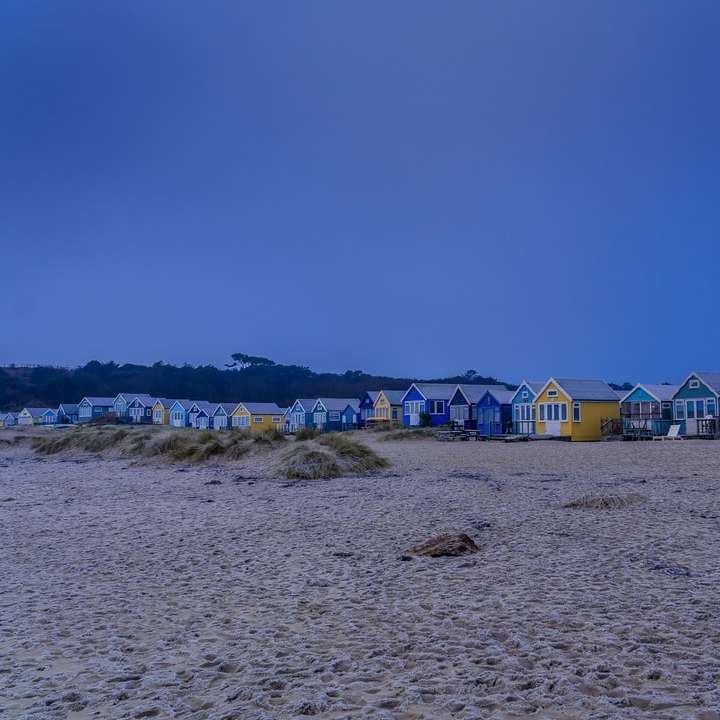 casă din lemn albastru și alb pe nisip maro sub cer albastru puzzle online
