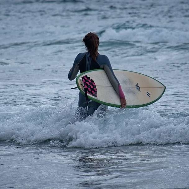 vrouw in zwarte en rode wetsuit rijden witte surfplank online puzzel