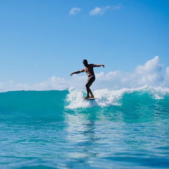 uomo in pantaloncini neri surf sul mare blu durante il giorno puzzle scorrevole online