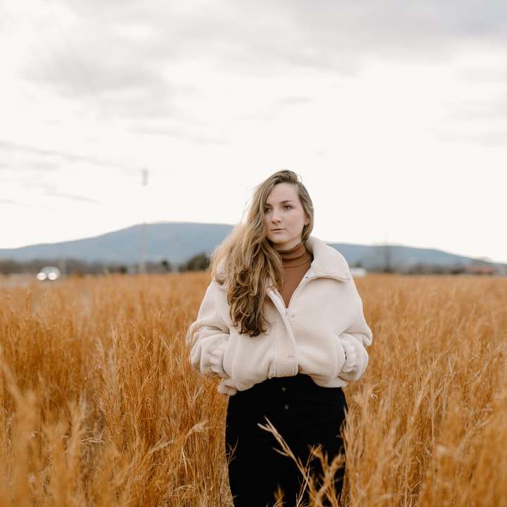 женщина в белой куртке стоит на поле коричневой травы онлайн-пазл