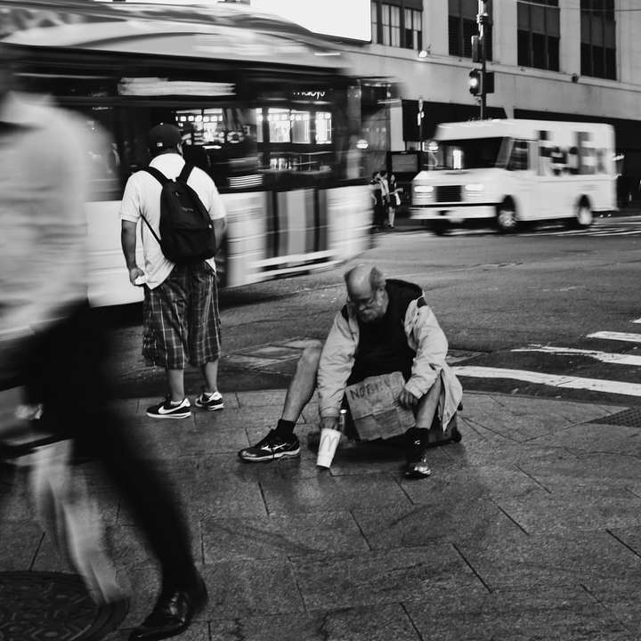 fotografie în tonuri de gri a unei femei în jachetă neagră așezată pe trotuar puzzle online