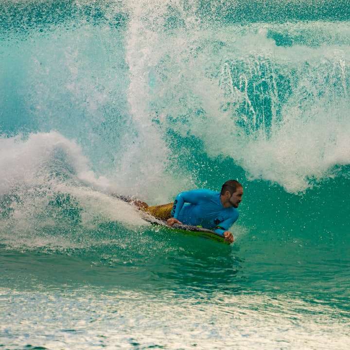 Hombre de camisa azul surfeando en las olas del mar durante el día rompecabezas en línea