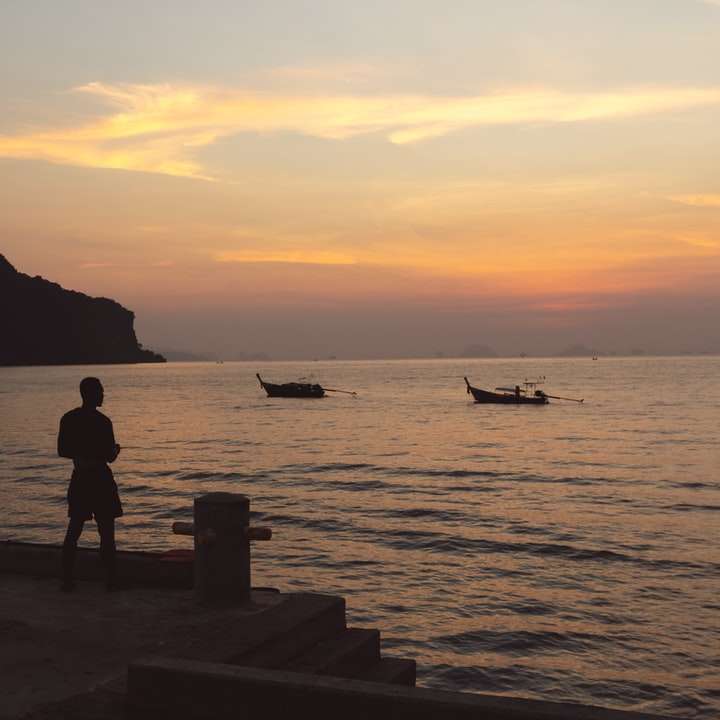 Silueta de persona de pie sobre un muelle de hormigón durante la puesta de sol rompecabezas en línea