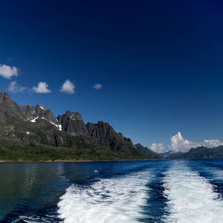 grönt berg bredvid vattnet under blå himmel glidande pussel online