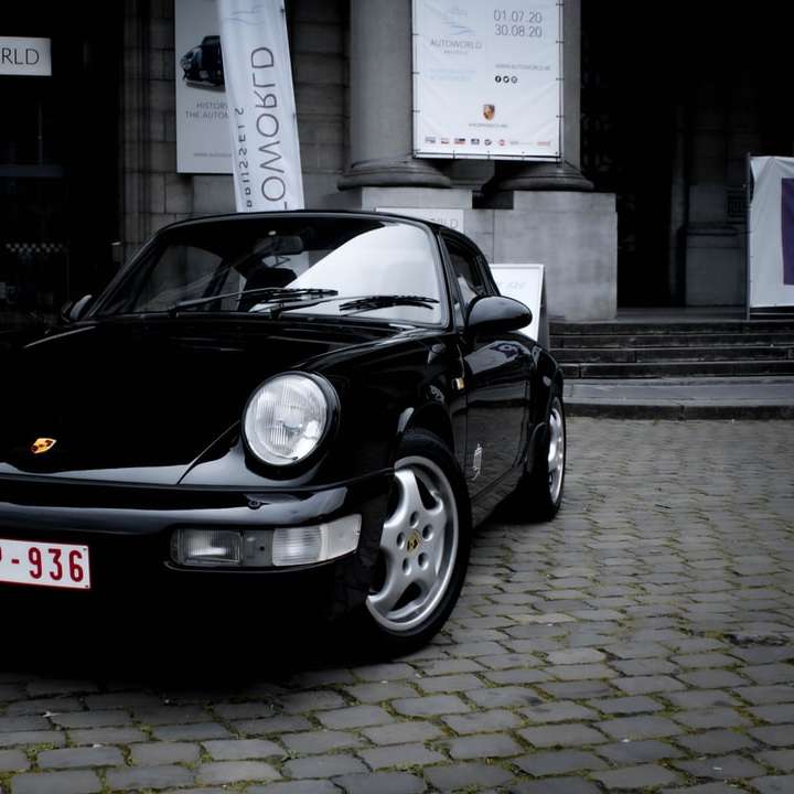 черно Porsche 911 паркирано върху сив тухлен под плъзгащ се пъзел онлайн