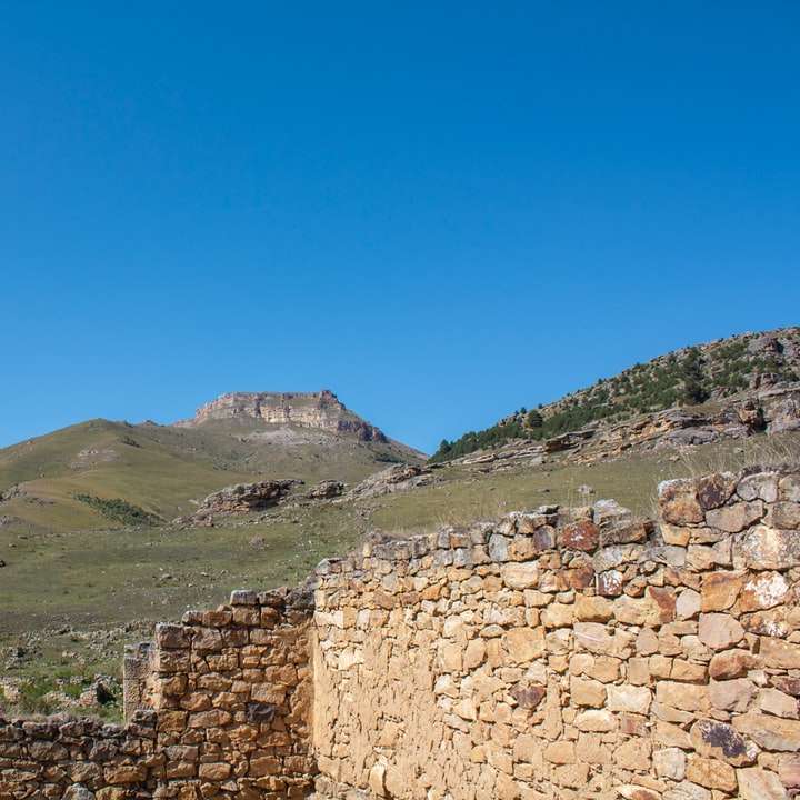 brązowy mur z cegły w pobliżu pola zielonej trawy i góry puzzle online