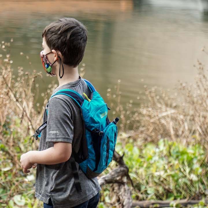 Junge im blauen und schwarzen Rucksack, der nahe dem Gewässer steht Online-Puzzle
