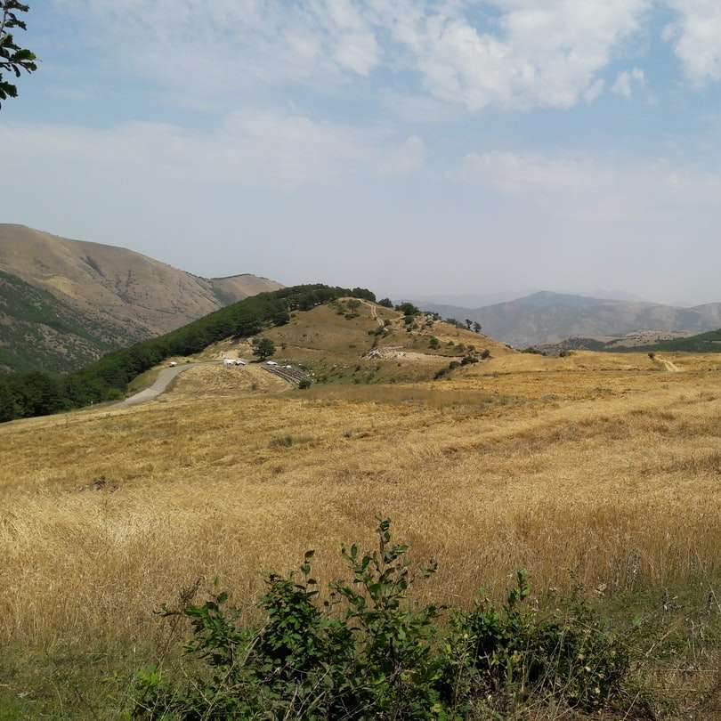fält för grönt gräs nära berg under vita moln Pussel online