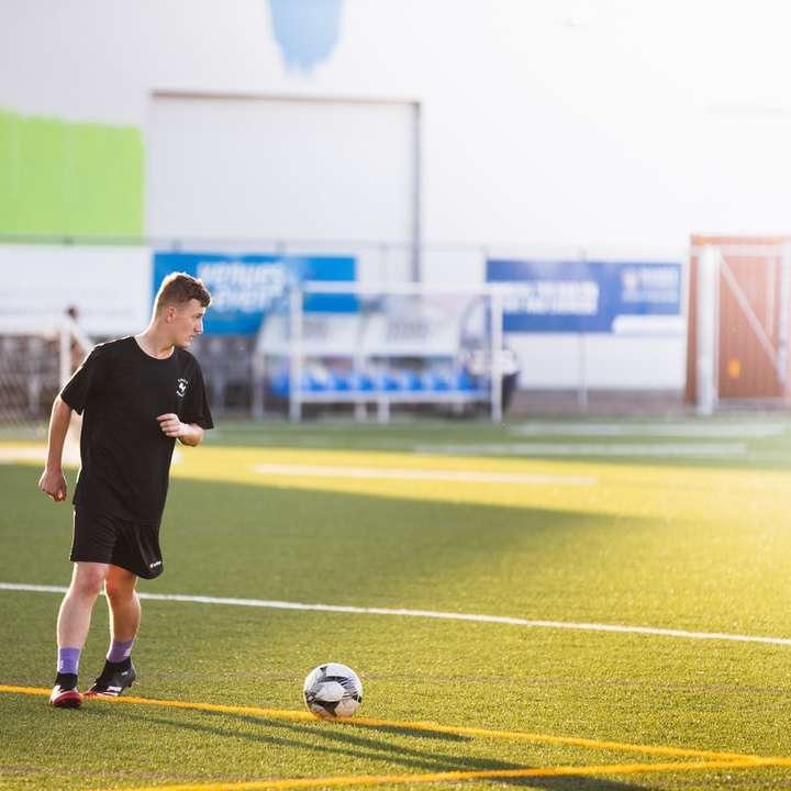 Hombre con camisa negra y pantalones cortos jugando al fútbol durante el día puzzle deslizante online