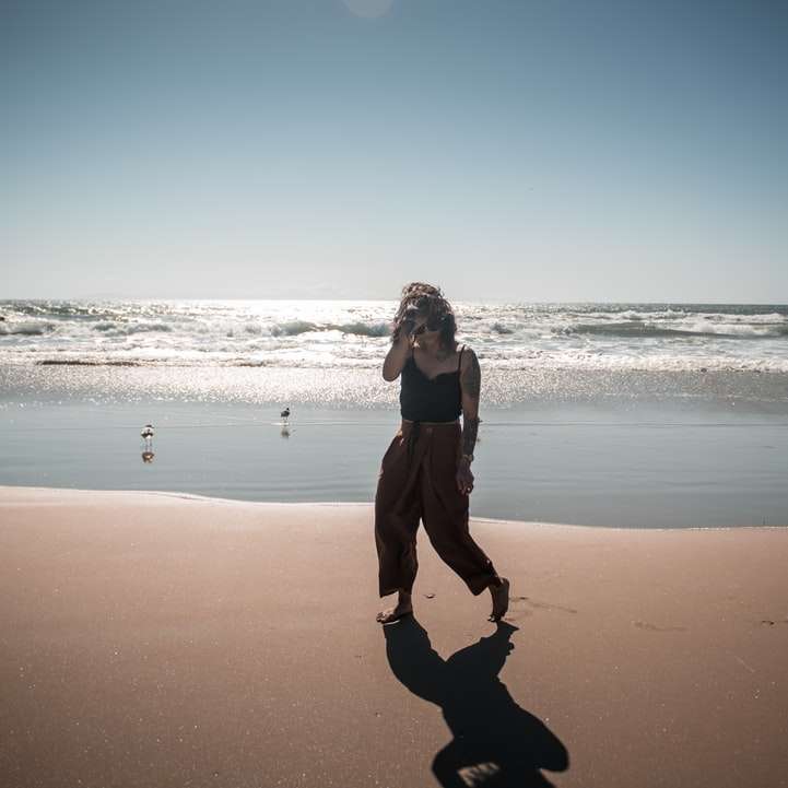 жена в черно яке и черни панталони, разхождащи се на плажа плъзгащ се пъзел онлайн