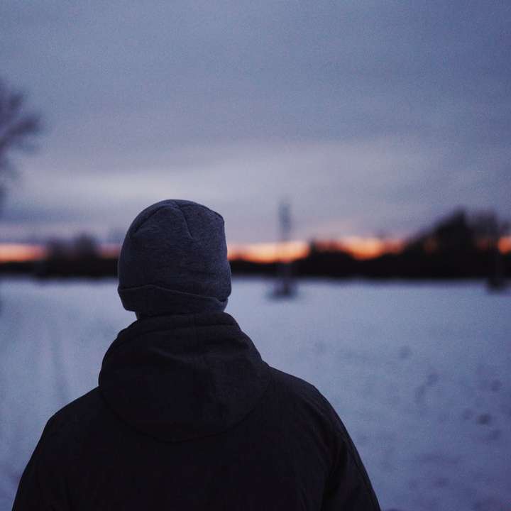 persona en sudadera con capucha negra de pie cerca del campo cubierto de nieve puzzle deslizante online