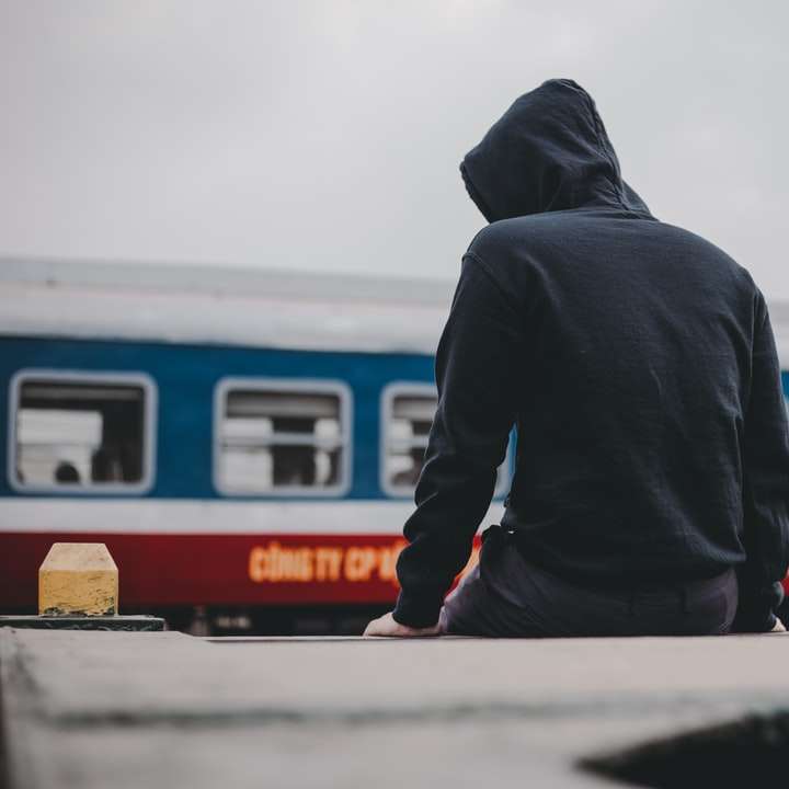 mężczyzna w czarnej bluzie z kapturem stojący w pobliżu pociągu biało-czerwonego puzzle online