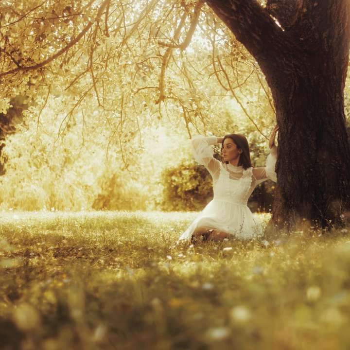 жена в бяла рокля, седнала на поле със зелена трева онлайн пъзел