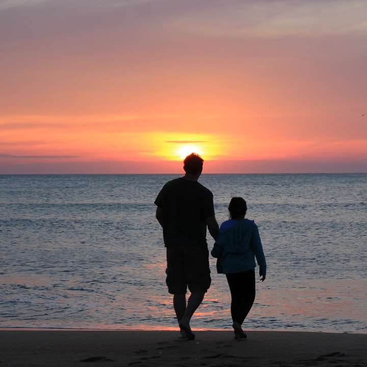мъж и жена, стоящи на плажа по време на залез онлайн пъзел