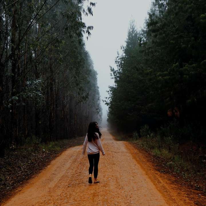 woman in black jacket walking on dirt road sliding puzzle online