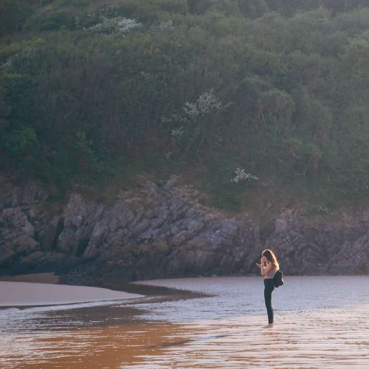 woman in black dress walking on brown sand near body sliding puzzle online