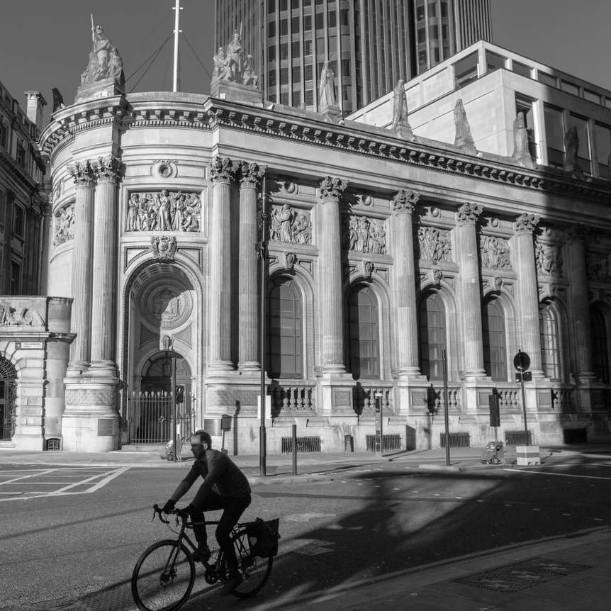 fotografie în tonuri de gri a omului călărind cu bicicleta pe drum lângă clădire puzzle online