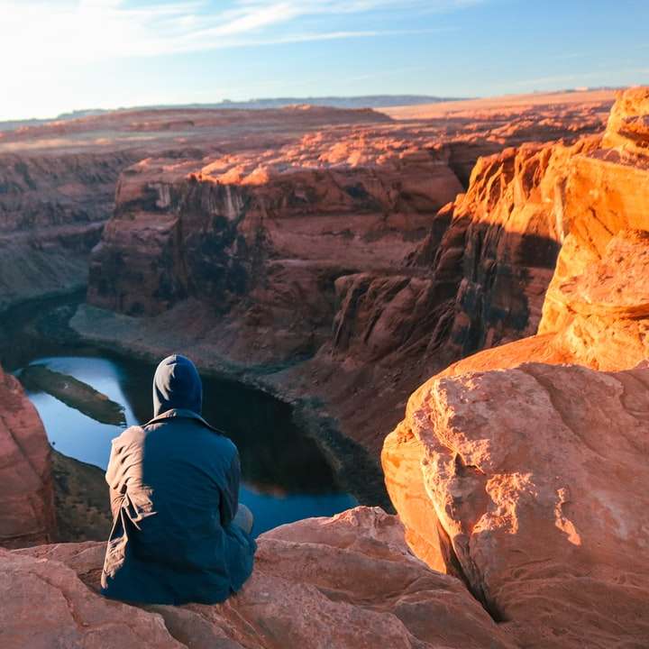 man in black jacket sitting on brown rock formation online puzzle