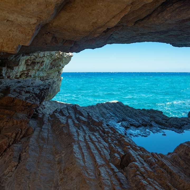 Formación de roca marrón cerca del mar azul durante el día puzzle deslizante online
