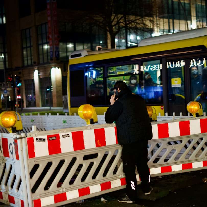 мъж в черно яке, стоящ до жълто-бял автобус онлайн пъзел
