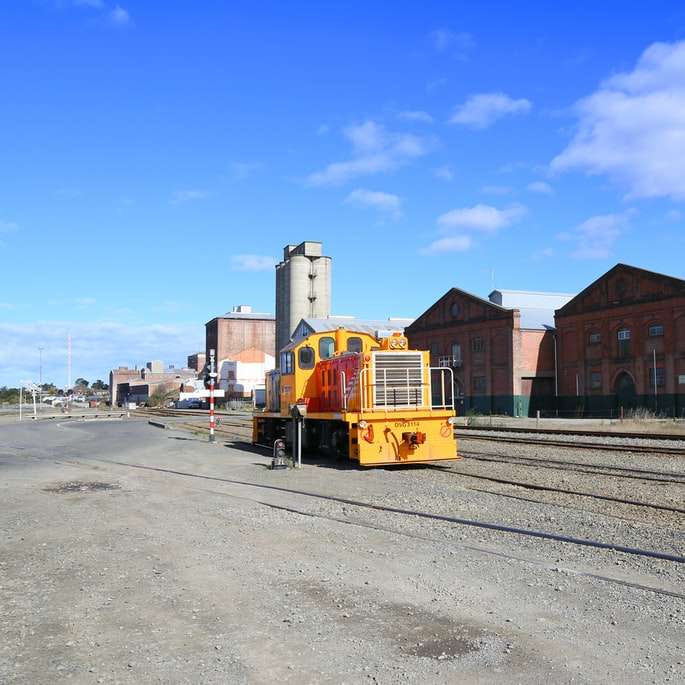 gult och svart tåg på järnvägsväg nära brun byggnad glidande pussel online