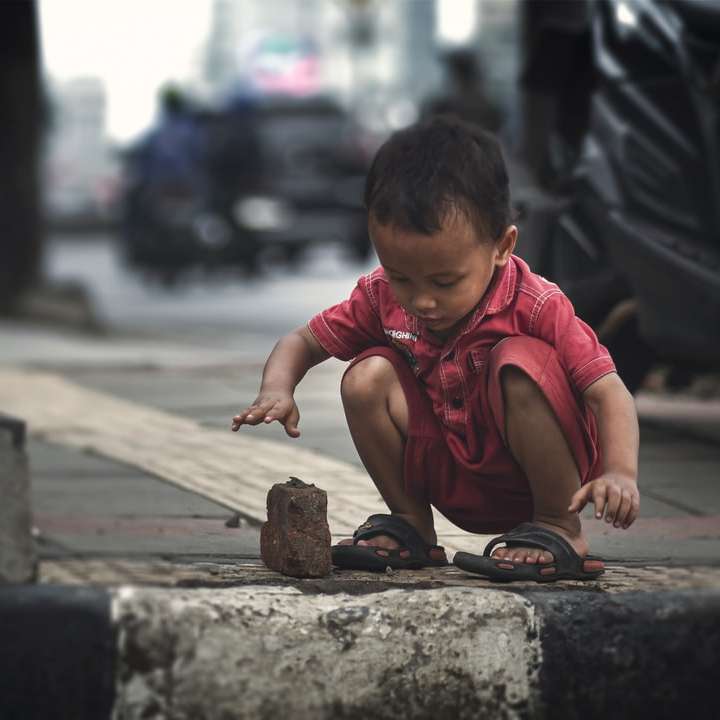 Garçon en t-shirt à col rond rouge assis sur un trottoir en béton puzzle coulissant en ligne