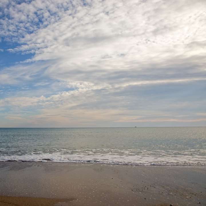 zee golven op de wal onder blauwe en witte bewolkte hemel schuifpuzzel online