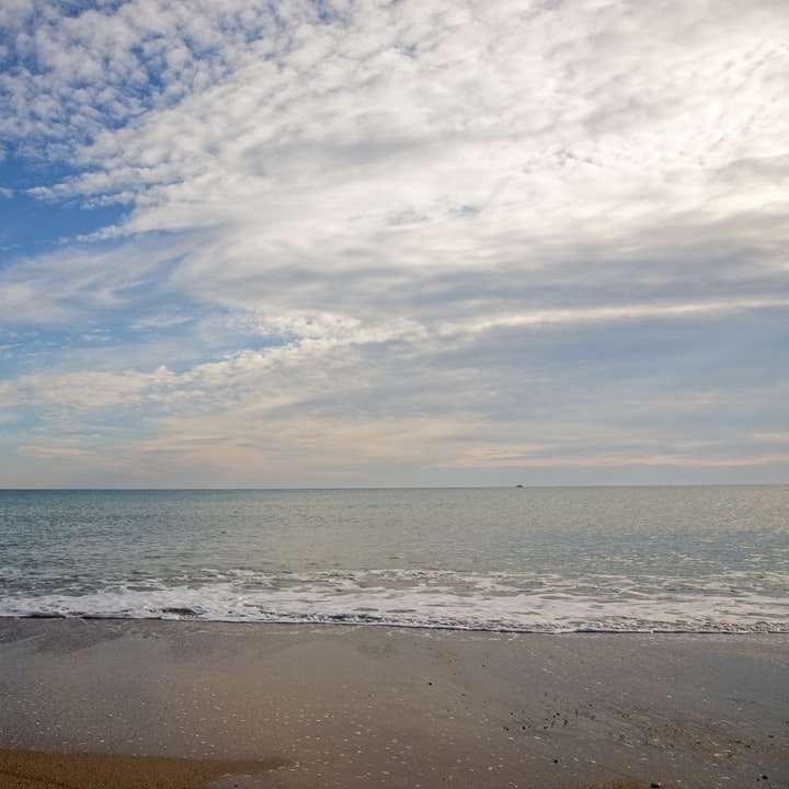 Meereswellen, die am Ufer unter blauem und weißem bewölktem Himmel krachen Schiebepuzzle online