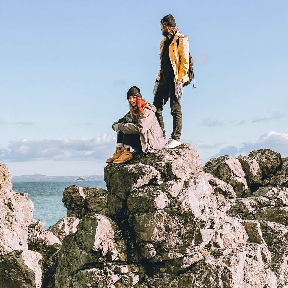 Paar sitzt auf Felsformation in der Nähe von Gewässern Online-Puzzle
