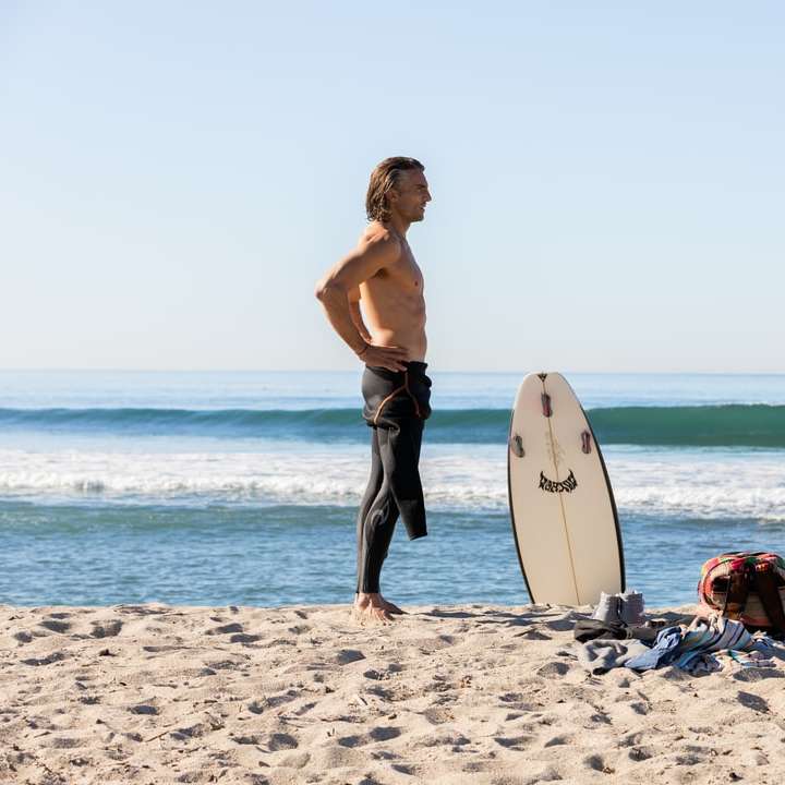 kvinna i blå jeansshorts som rymmer den vita surfbrädan på stranden glidande pussel online