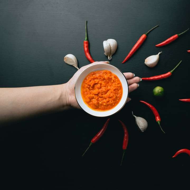 Person, die weißen Keramikbecher mit rotem und grünem Chili hält Online-Puzzle