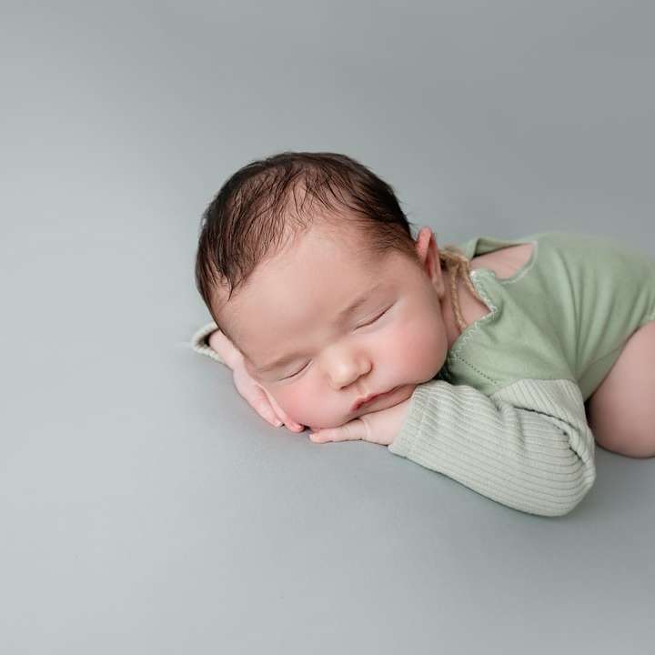 baby in groen shirt liggend op wit textiel online puzzel