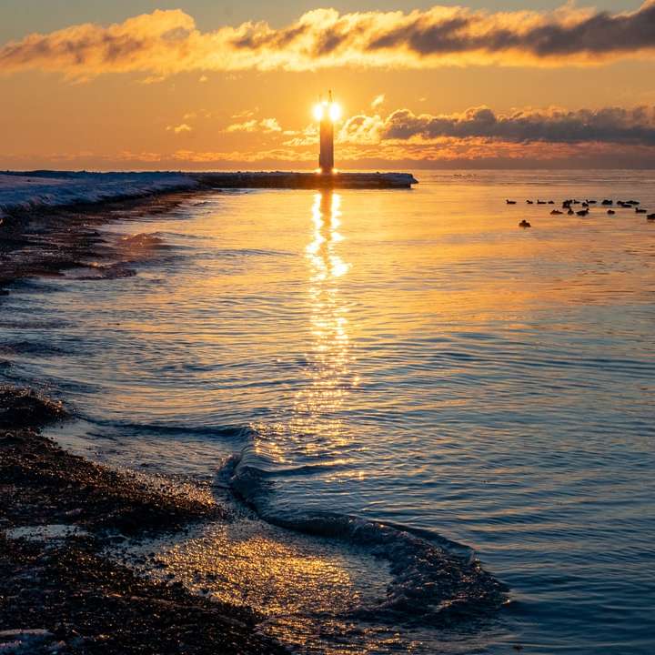 silueta del faro en la playa durante la puesta de sol puzzle deslizante online