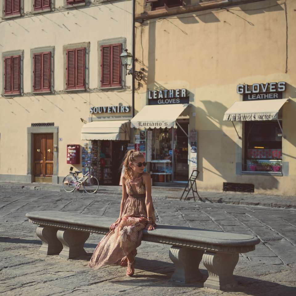 жінка в коричневій сукні, сидячи на лавці біля будівлі онлайн пазл