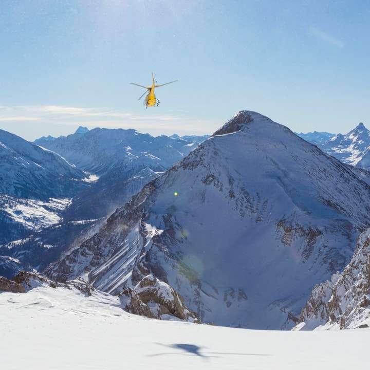 雪に覆われた山の上を飛んでいる黄色と黒のヘリコプター スライディングパズル・オンライン