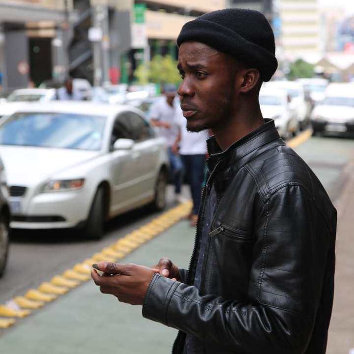 man in black leather jacket standing on sidewalk sliding puzzle online
