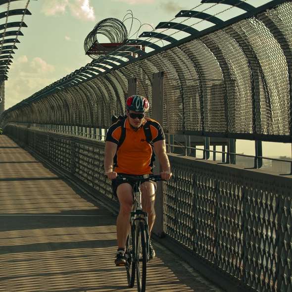 мъж в оранжева риза, каращ велосипед на мост през деня онлайн пъзел