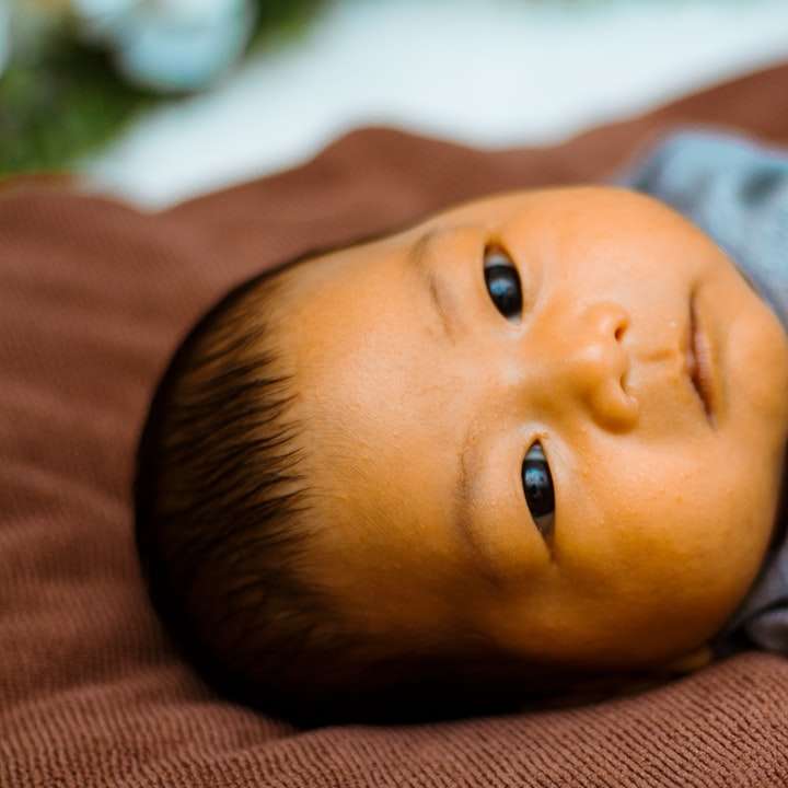 bebis i grå skjorta som ligger på brun textil glidande pussel online