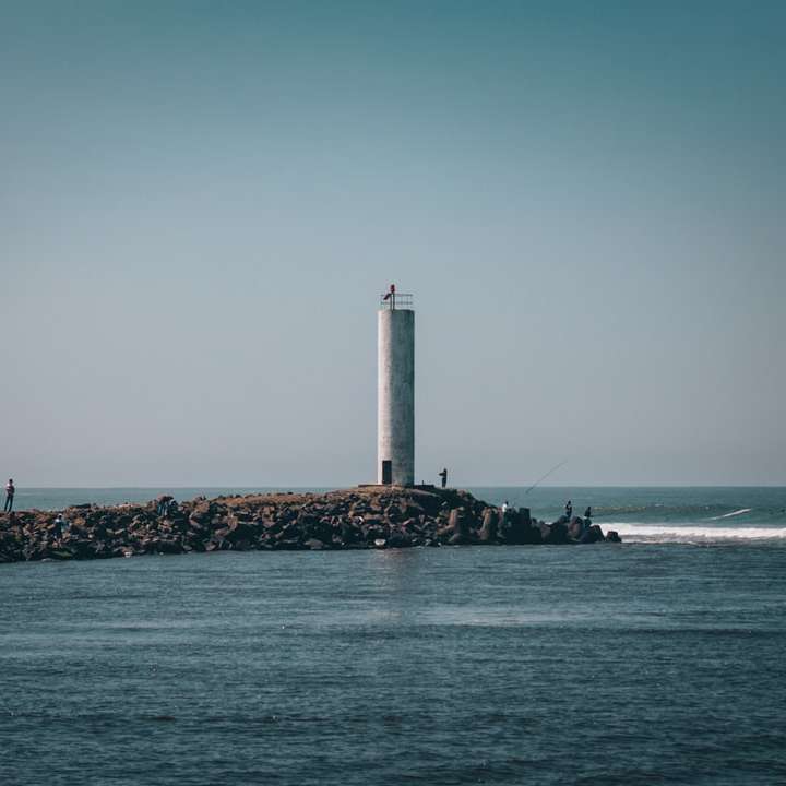 昼間の茶色の岩の多い海岸にある白い灯台 オンラインパズル