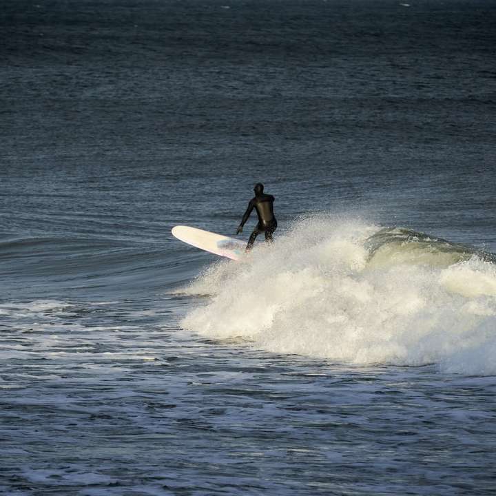 мъж в черен мокър костюм, яздящ бял сърф на морски вълни плъзгащ се пъзел онлайн