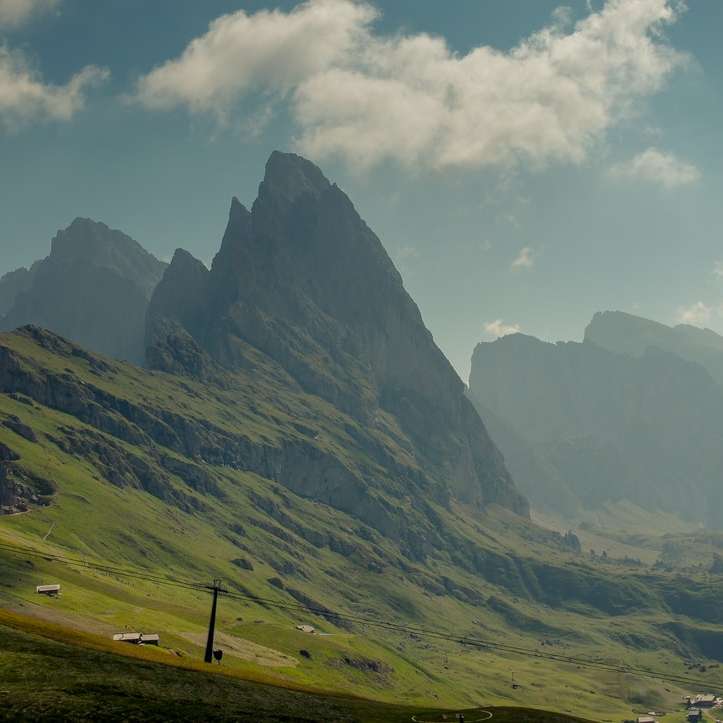 πράσινο γρασίδι πεδίο κοντά στο βουνό κάτω από άσπρα σύννεφα συρόμενο παζλ online