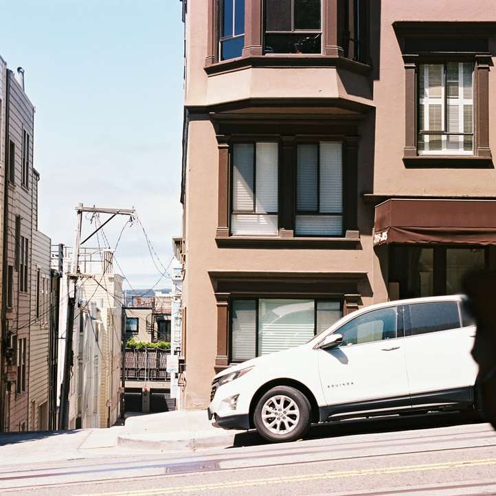Белая машина припаркована рядом с коричневым бетонным зданием онлайн-пазл