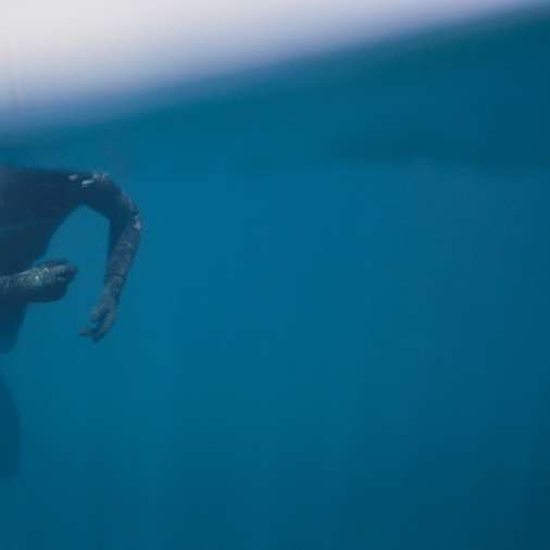 Person im schwarzen Neoprenanzug, der im Meer schwimmt Schiebepuzzle online