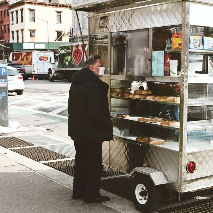Человек в черной куртке стоит перед продуктовым ларьком онлайн-пазл