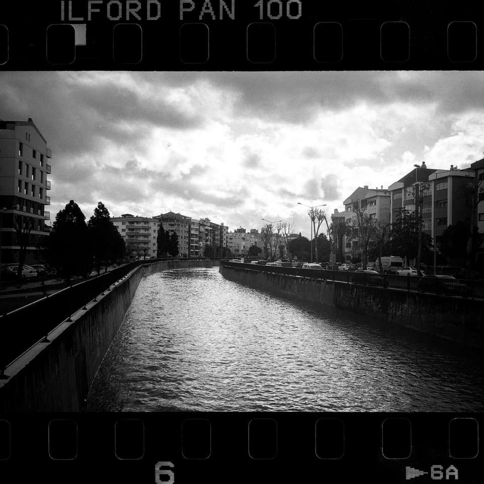 grayscale photo of river between buildings sliding puzzle online
