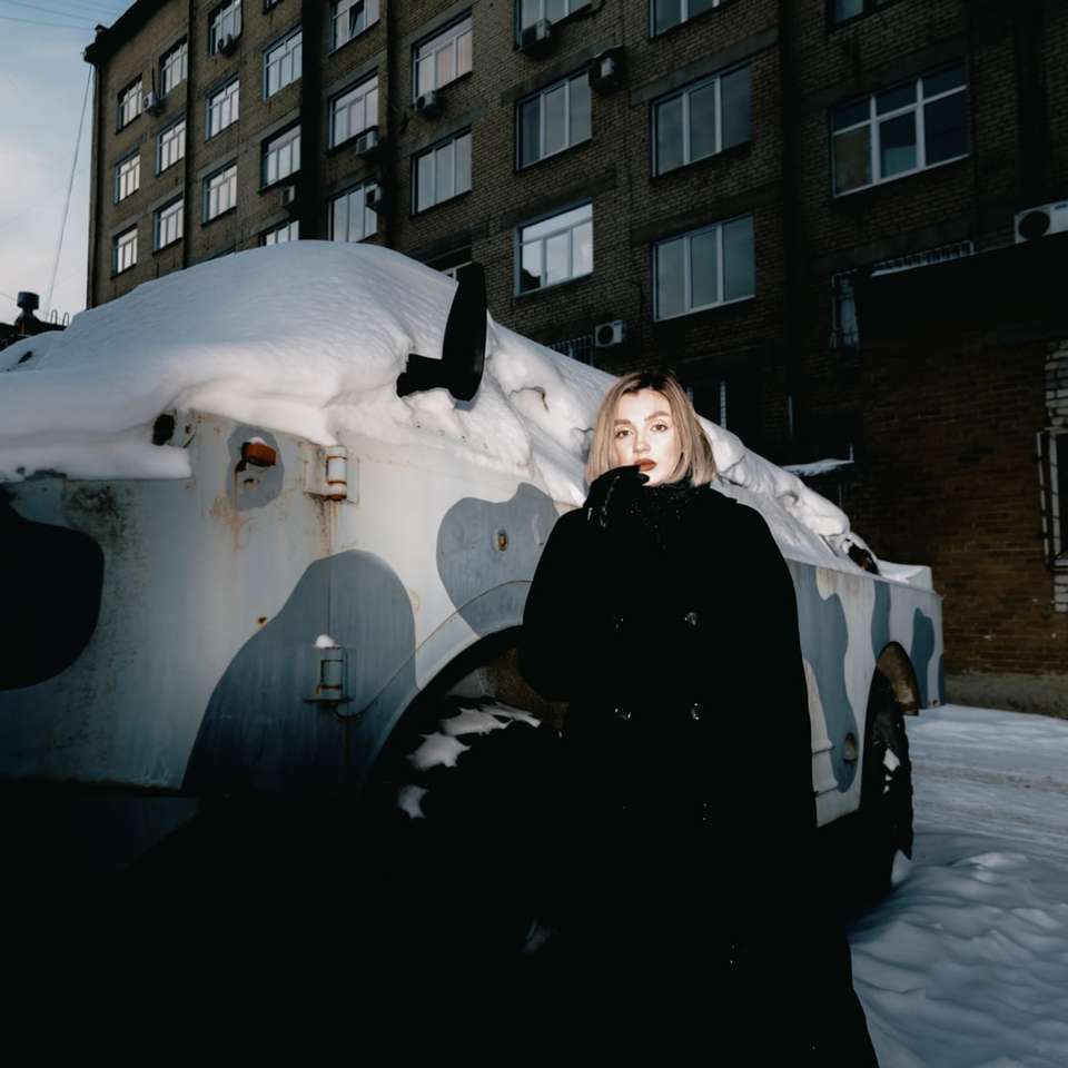 雪に覆われた地面に立っている黒いコートの女性 オンラインパズル