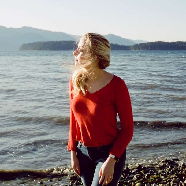 woman in red long sleeve shirt standing on rocky shore sliding puzzle online
