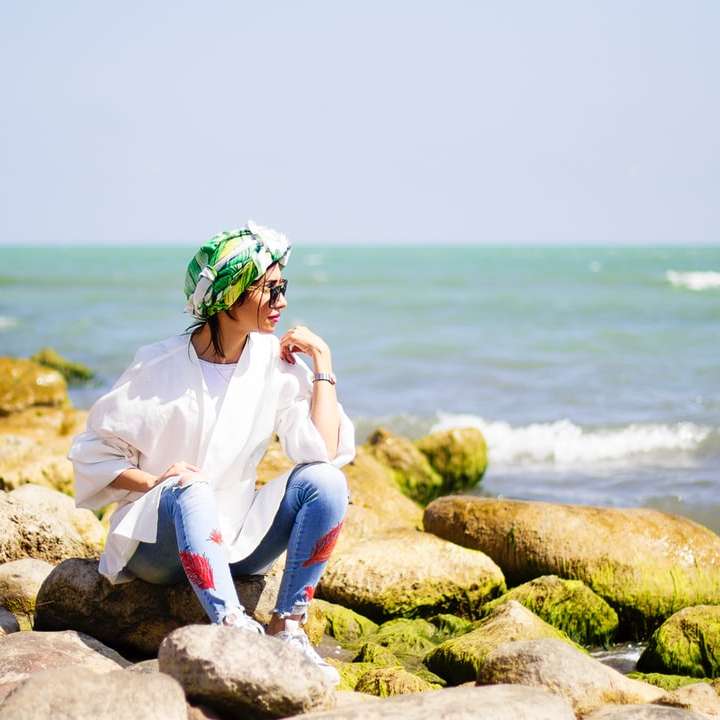 žena v bílé košili s dlouhým rukávem, sedící na skále poblíž moře online puzzle